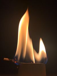 Close-up of burning candle against black background