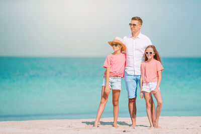Full length of girls with father on beach against sky
