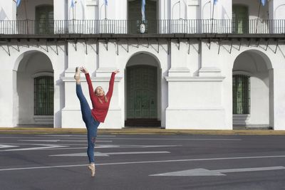 Full length of young woman dancing on road in city