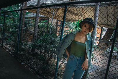 Portrait of smiling young woman standing by fence