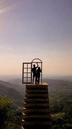 Rear view of couple standing on staircase against sky during sunset