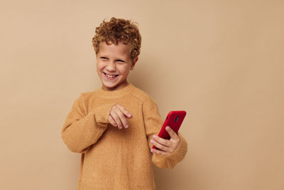 Boy holding smart phone against beige background