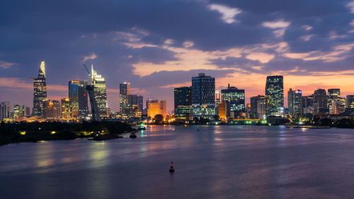 Illuminated buildings by river against sky