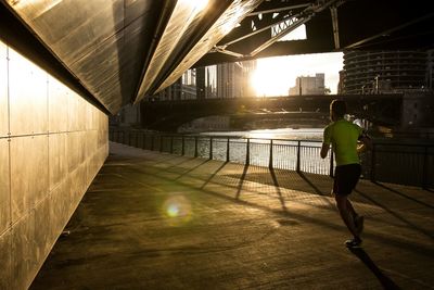 Full length rear view of man running on bridge during sunny day