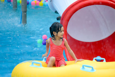 Cute girl looking away while sitting in inflatable ring on swimming pool