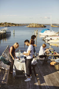 Young multi-ethnic friends preparing lunch at harbor against sky on sunny day