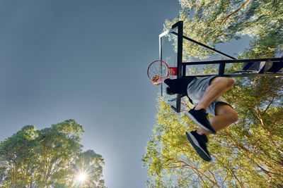 Low angle view of man putting ball in basketball hoop against clear sky