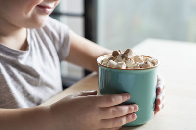 Midsection of woman holding coffee cup on table at home