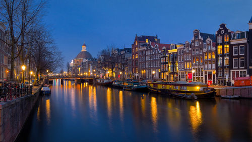 River amidst illuminated buildings against sky at dusk