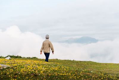 Back view of unrecognizable senior female traveler walking in morning in hilly terrain