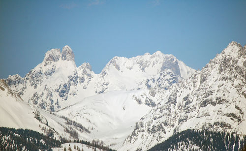 Low angle view of snowcapped mountains against clear blue sky