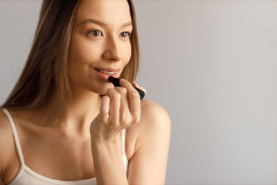 Close-up of young woman applying lipstick against wall