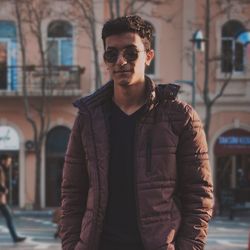 Young man wearing sunglasses standing against buildings in city