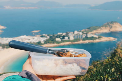 Cropped image of person holding adobo container against sea at cape daguilar