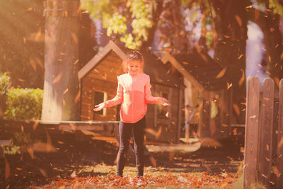 Full length of girl standing below falling leaves at backyard during autumn