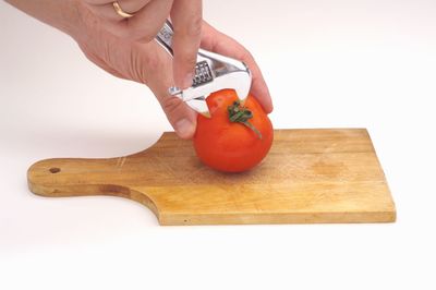 Cropped image of hand holding orange slice on cutting board