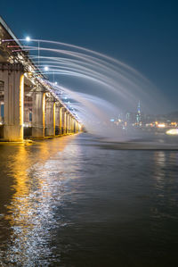 Illuminated bridge over river in city at night