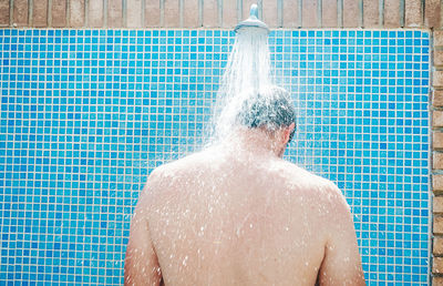 Rear view of man standing by shower outdoors