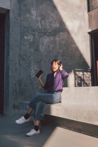 Full length portrait of woman sitting on wall