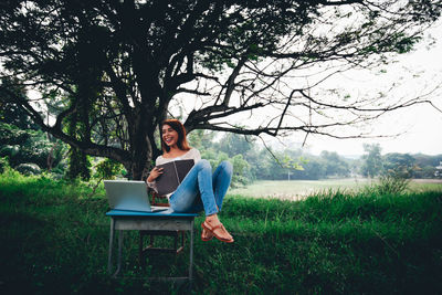 Happy young woman using laptop on table in park