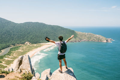 Rear view of young woman standing by sea against clear sky