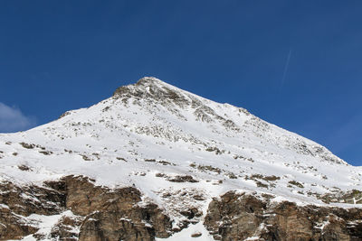 Low angle view of snowcapped mountains against blue sky