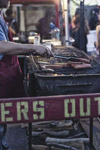 Cropped image of vendor roasting sausages on barbecue