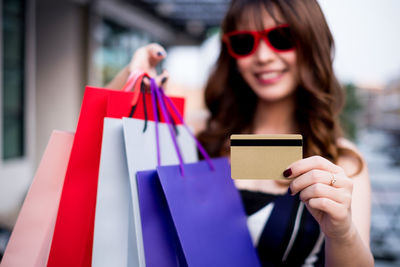 Smiling young woman holding shopping bags and credit card in city