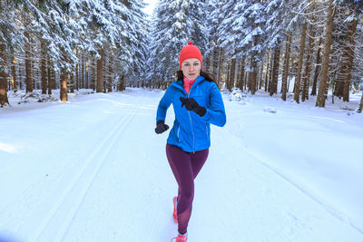 Portrait of mid adult woman running on snow covered field against trees in forest