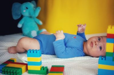 Cute baby boy lying by toys on bed at home