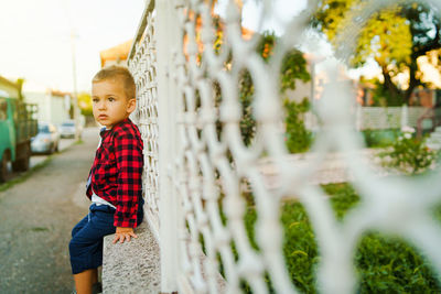 Cute boy looking away while sitting on retaining wall