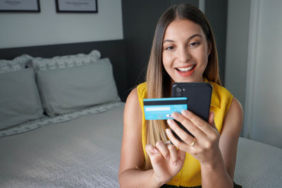 Joyful excited young woman doing online transaction with her smartphone and credit card from home. 