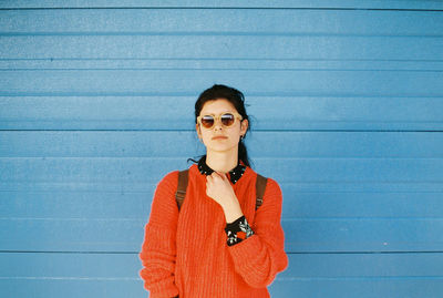 Portrait of woman wearing sunglasses while standing against blue wall