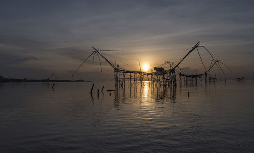 Silhouette of fishing net in sea against sunset sky