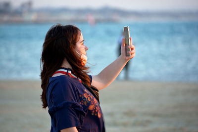 Side view of young woman with arms outstretched standing at beach