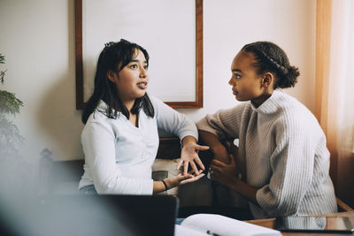 Teenage girl gesturing while talking to friend on sofa in living room