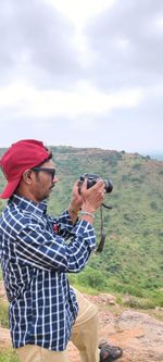 Side view of man photographing while standing on field against sky