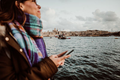 Young woman using mobile phone in sea against sky