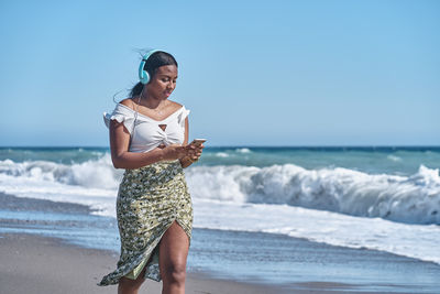 Young african american woman listening to music by the shore of the beach