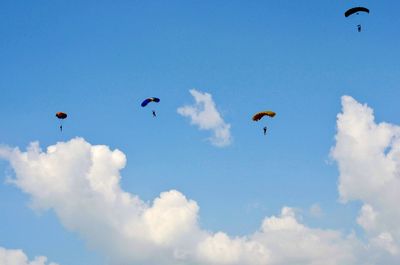 Low angle view of people paragliding against sky