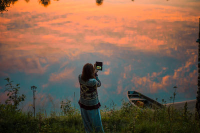 Rear view of woman photographing lake with clouds reflection at sunset