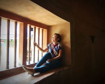 Full length of woman sitting on window sill