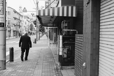 Rear view full length of man walking on sidewalk in city