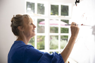 Senior woman painting picture on canvas at home