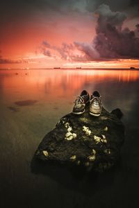 Close-up of shoes on shore against sky during sunset