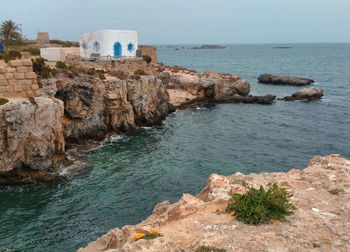 Scenic view of sea and small house on rocks against clear sky