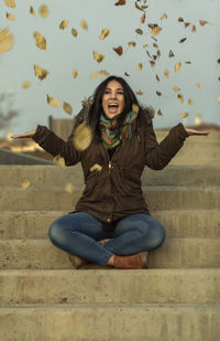 Full length of happy young woman sitting outdoors