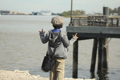 Rear view of boy gesturing while standing at beach