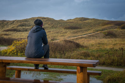 Man sitting on bench over field against sky