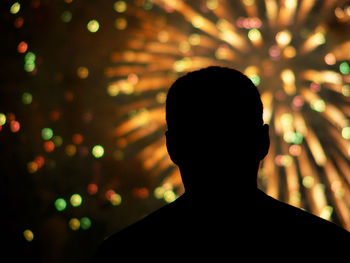 Rear view of silhouette man against firework display at night